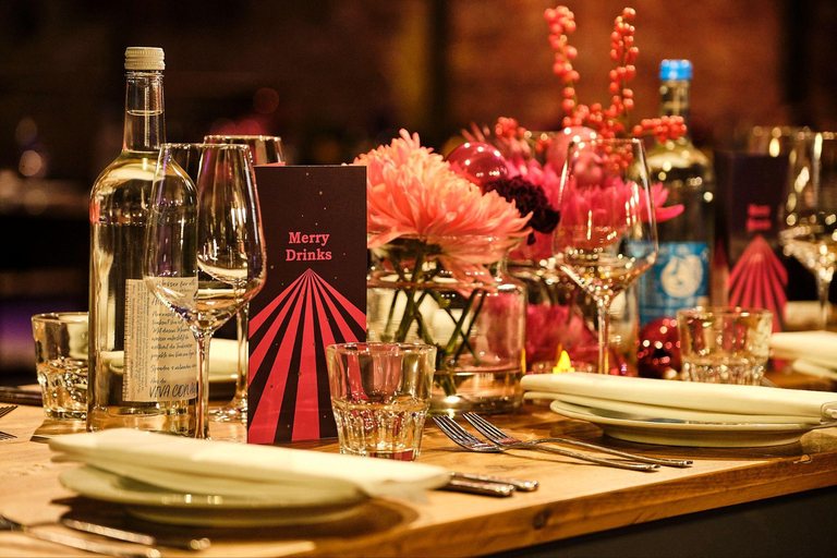 Festlich gedeckte Tafel mit roten Weihnachtskugeln, Blumen und Gläsern im warmen Licht