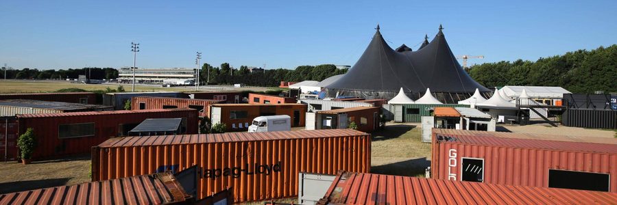 Container-Architektur und Zeltdächer der Tagungsflächen vor blauem Himmel