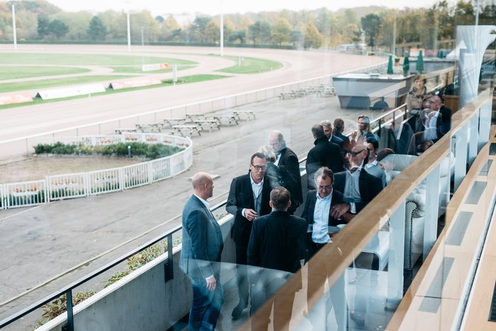 Geschäftsgäste auf dem Balkon des Tribünengebäudes über der Rennbahn