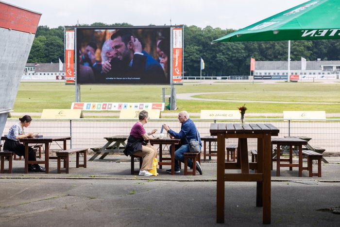 Gäste an Biertischen am Infield mit Großbildleinwand an der MIGNON Trabrennbahn