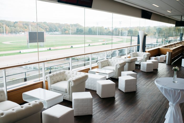 Weiße Lounge mit Panoramafenstern und Blick auf die Rennbahn der MIGNON Trabrennbahn