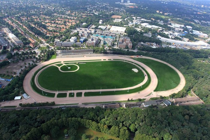 Luftbild des grünen Ovals der MIGNON Trabrennbahn mit Volkspark und Stadt im Hintergrund