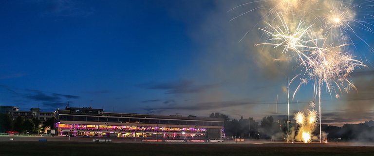 Feuerwerk über dem beleuchteten Tribünengebäude der MIGNON Trabrennbahn bei Nacht