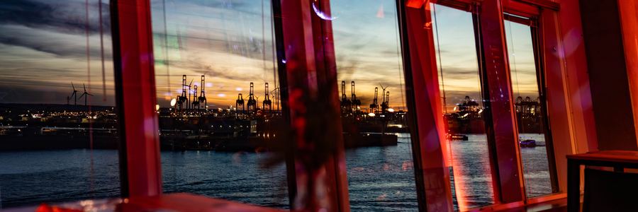 Rot beleuchtete Panoramafenster der Hafen Location mit Blick auf die Hamburger Hafenskyline am Abend