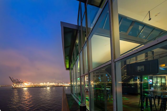 Gläserne Fassade der Hafen Location mit Hafenblick in der blauen Stunde
