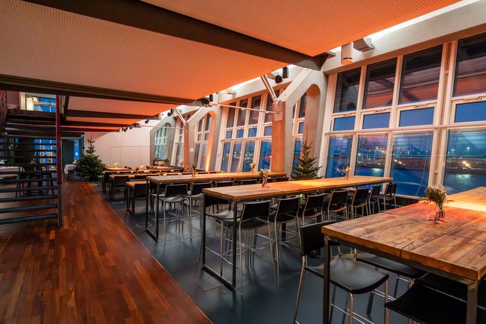 Warmer Innenraum der Hafen Location mit langen Holztischen und Elbblick im Sonnenuntergang