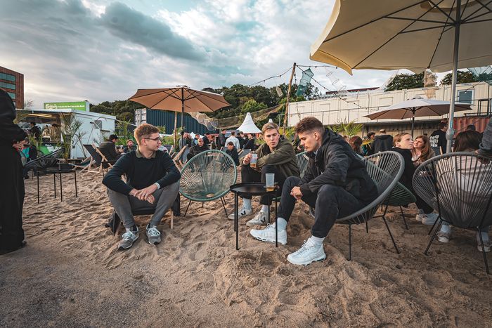 Gäste entspannen in Lounge-Sesseln im Sand am Platz am Fischereihafen in Hamburg