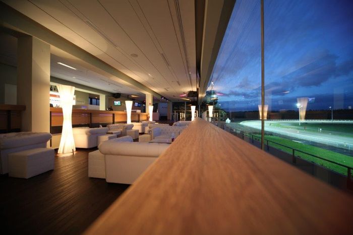 Lounge mit Panoramablick auf die beleuchtete Trabrennbahn in der Dämmerung
